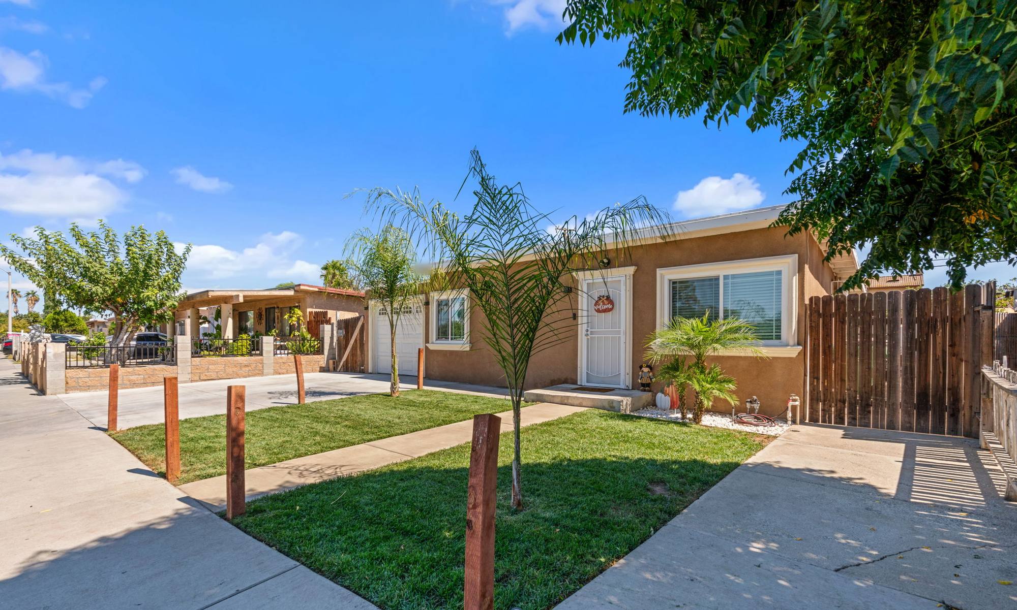 Single-story stucco home with young palm trees and a new front lawn